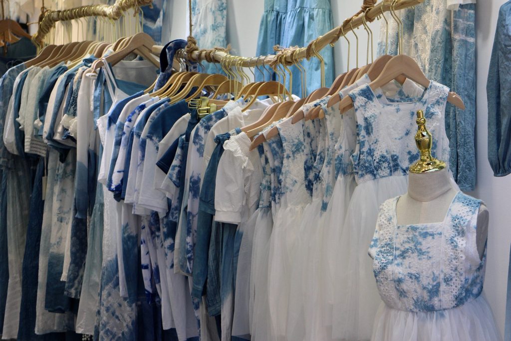 picture of an aesthetic boutique's clothing rack where the rack is made of natural wood. Clothes are all white and denim blue spotted hung on wooden clothes hangers.